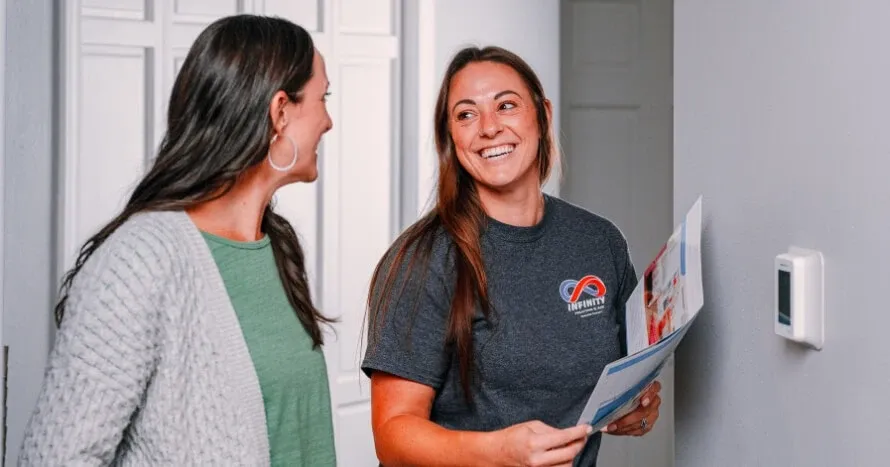 Two women converse happily in a hallway, discussing home energy efficiency improvements.