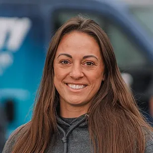 Smiling woman with long hair standing in front of a blue service vehicle, promoting excellence in customer service.