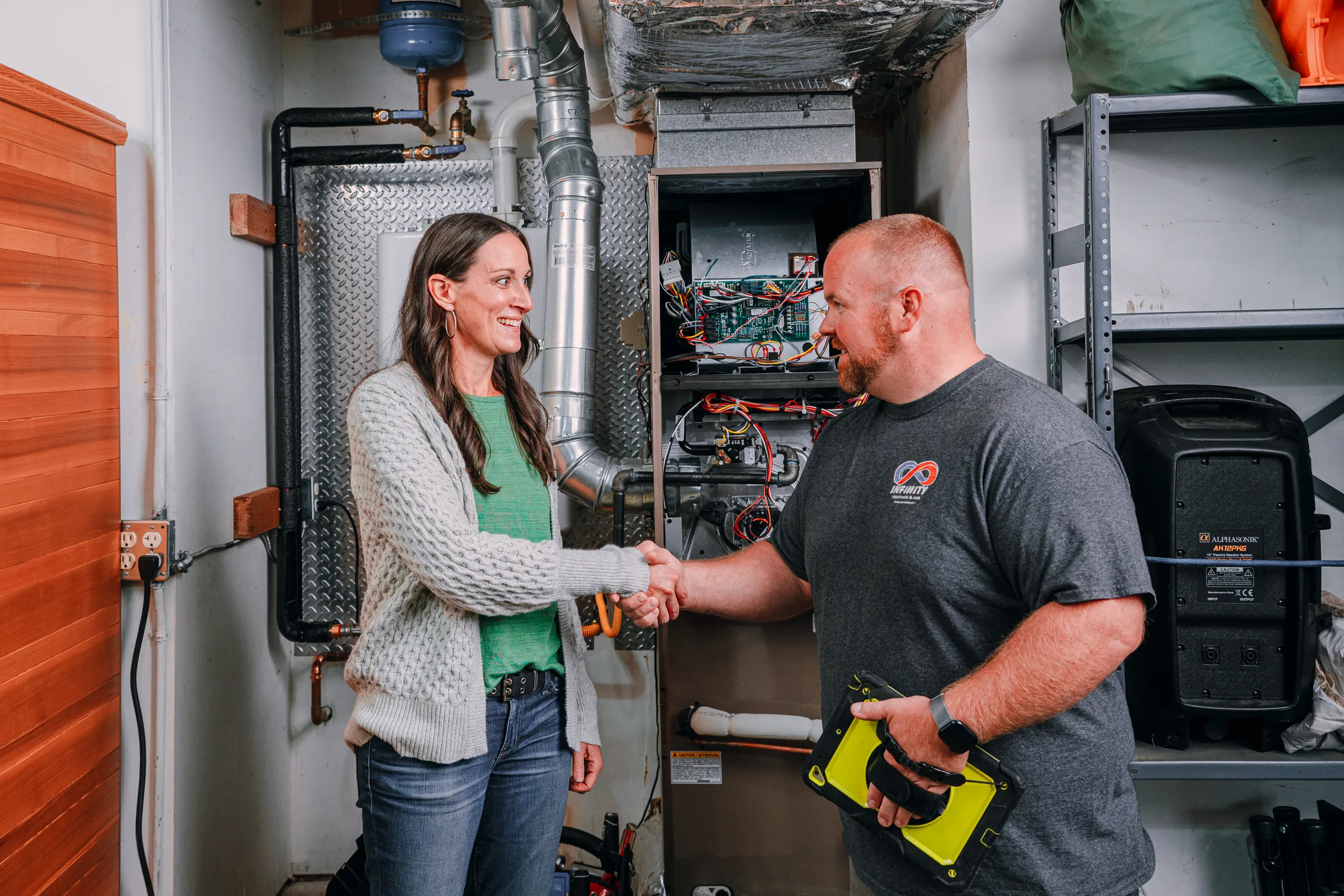A technician and a homeowner shake hands in a well-equipped basement, discussing HVAC maintenance.
