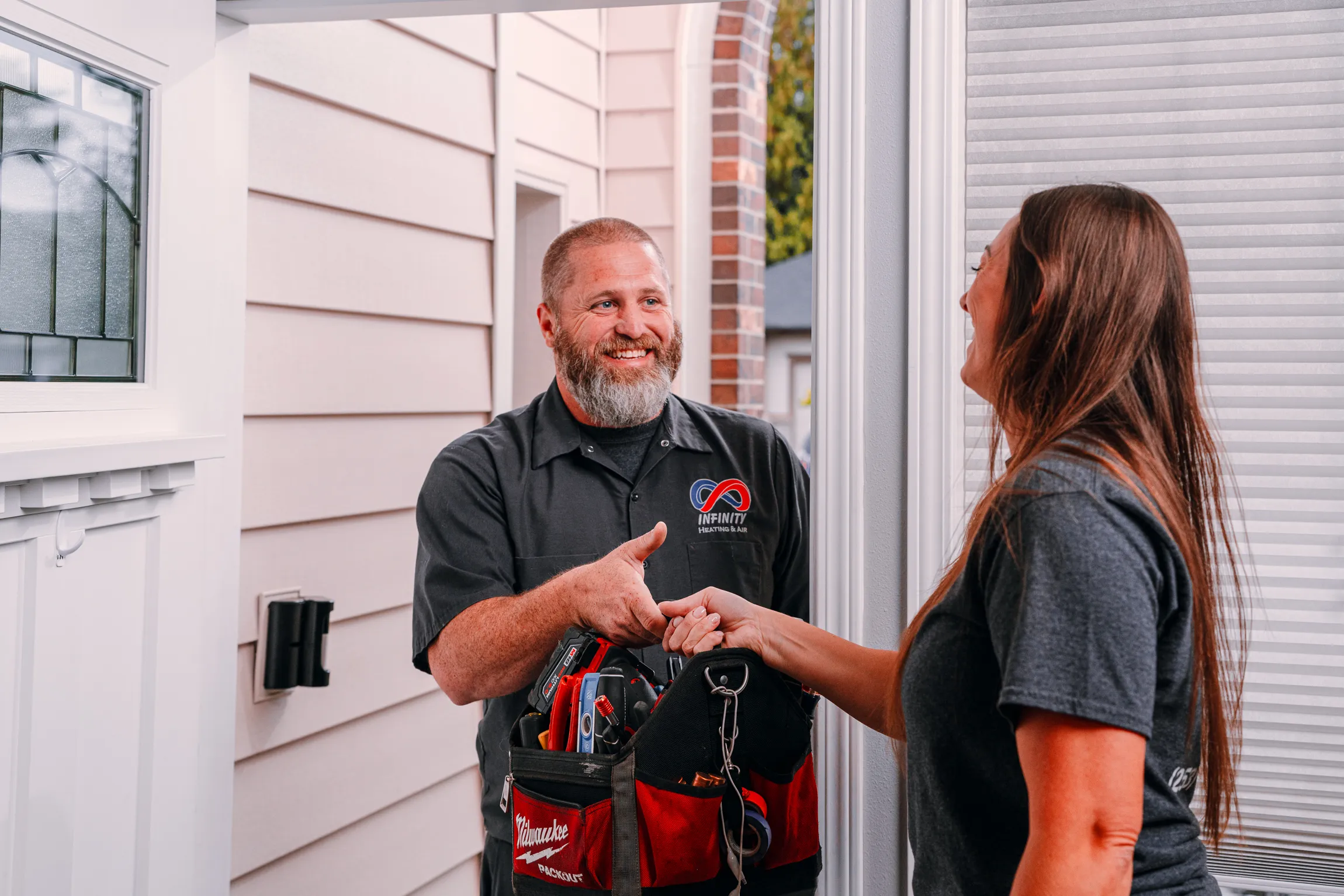A technician from Infinity Heating & Air greets a homeowner at the door with a friendly handshake.
