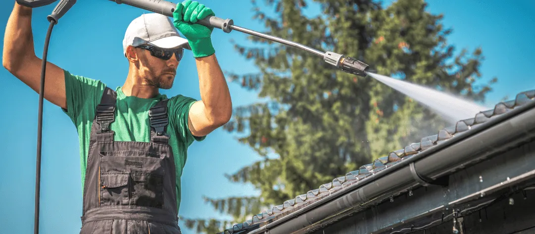  Worker using power washer for exterior surface cleaning on commercial building roof