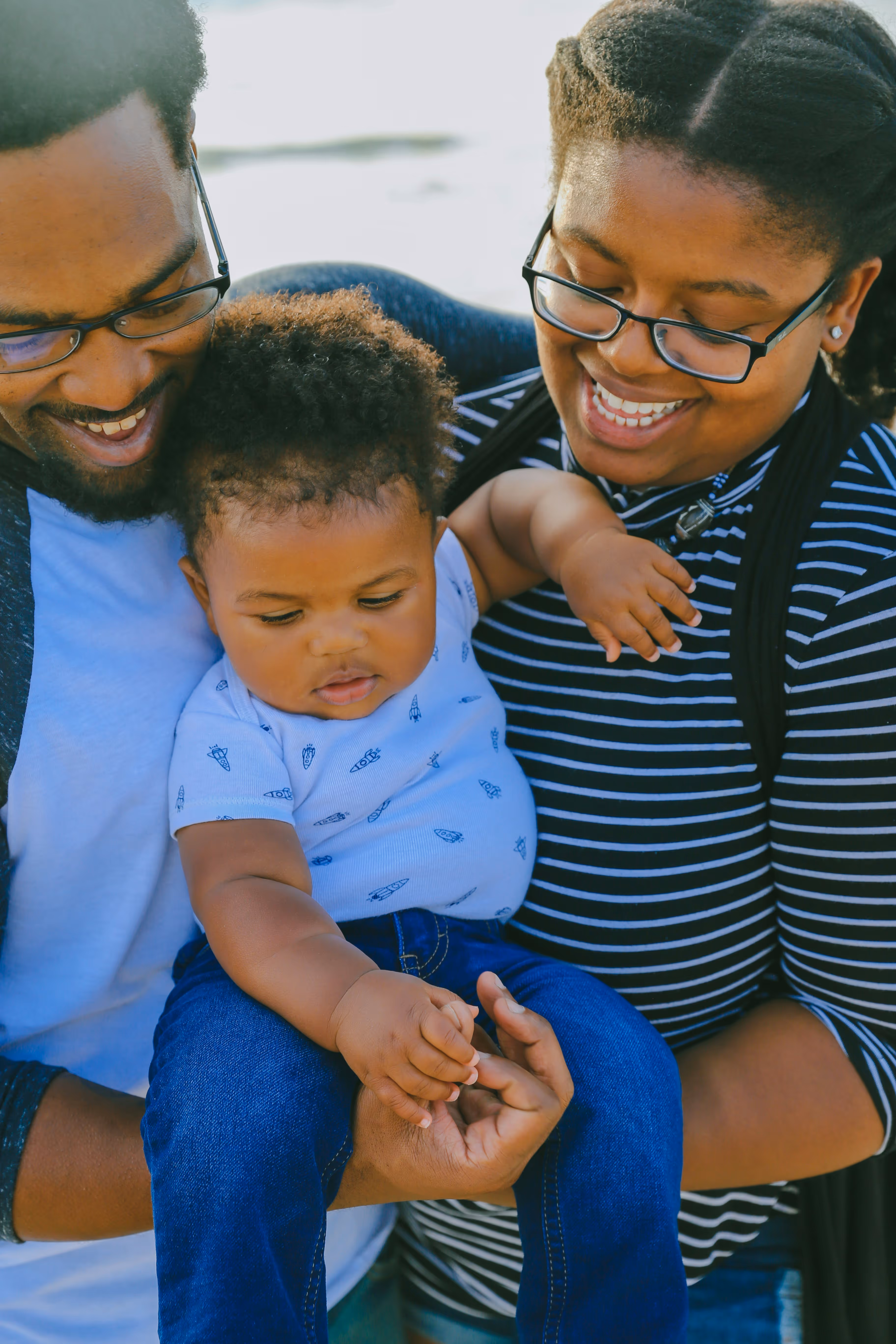 Smiling parents holding their baby outdoors, symbolizing family connection, support, and well-being.