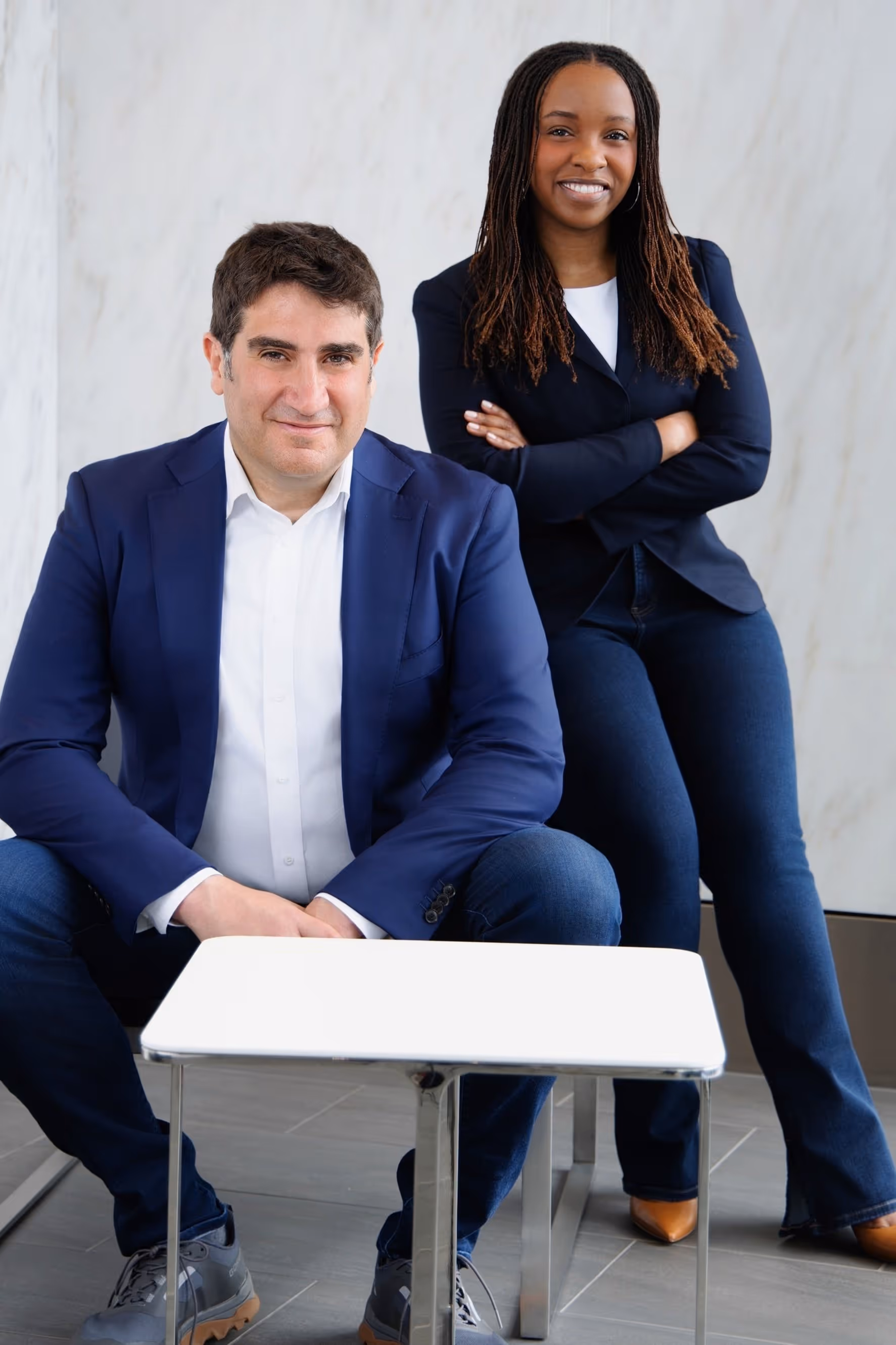 Photo of Jazmine and Andy, Quilt founders posing together in a bright, modern setting, both wearing business attire and smiling confidently