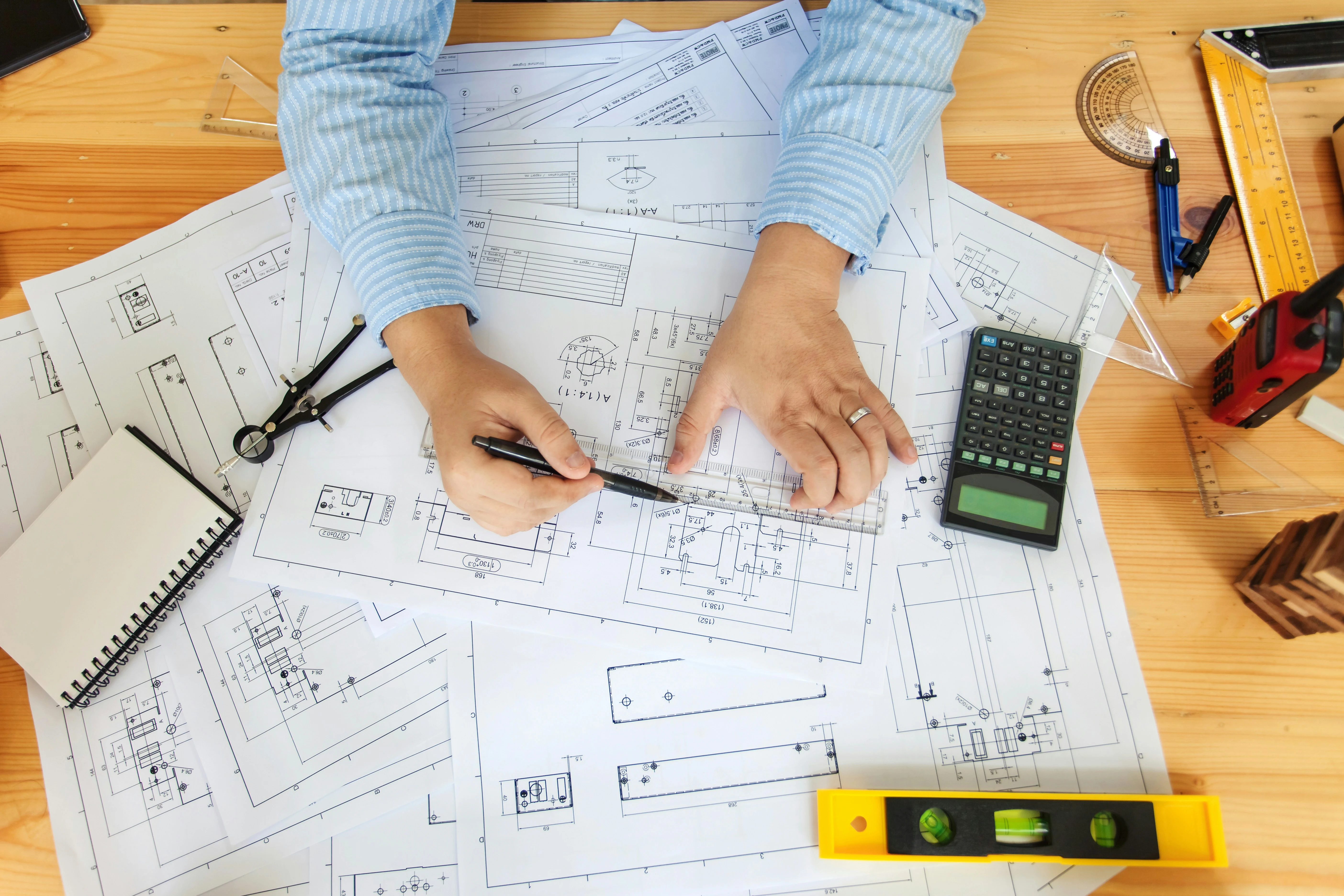Hands of a construction professional, pricing a job using technical drawings and a calculator