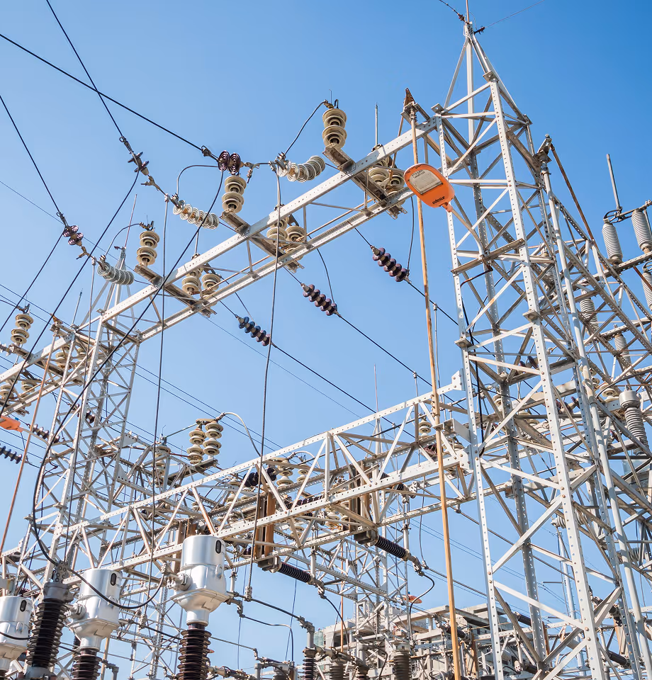 Metal framework and electrical insulators of a high-voltage electrical substation against a clear blue sky.