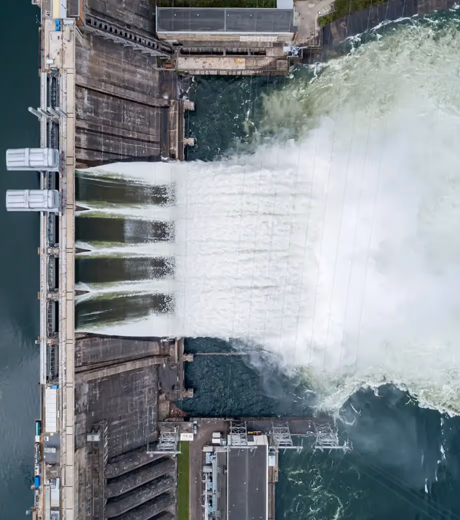 Aerial view of a dam releasing a large volume of water through its spillways into a river below.