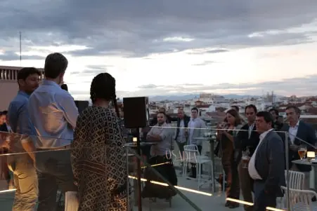Group of people gathered on a rooftop terrace during sunset with cityscape in the background.