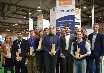 Group of people standing indoors at an event, holding wooden trophies in front of an Enerfip booth.