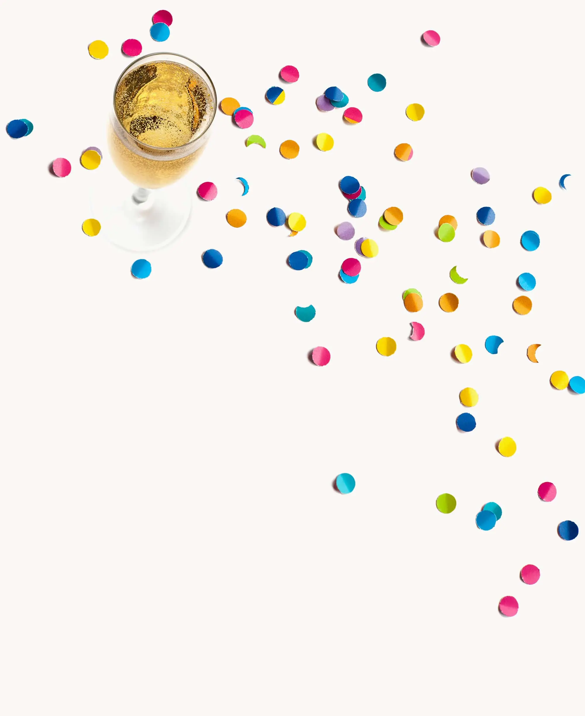 Glass of sparkling champagne surrounded by scattered colorful confetti on a white background.