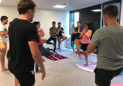 Group of people practicing yoga indoors, standing on one leg with hands in prayer position.