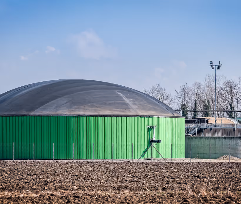 Large green biogas storage tank with a domed roof situated on a farm field under a clear sky.