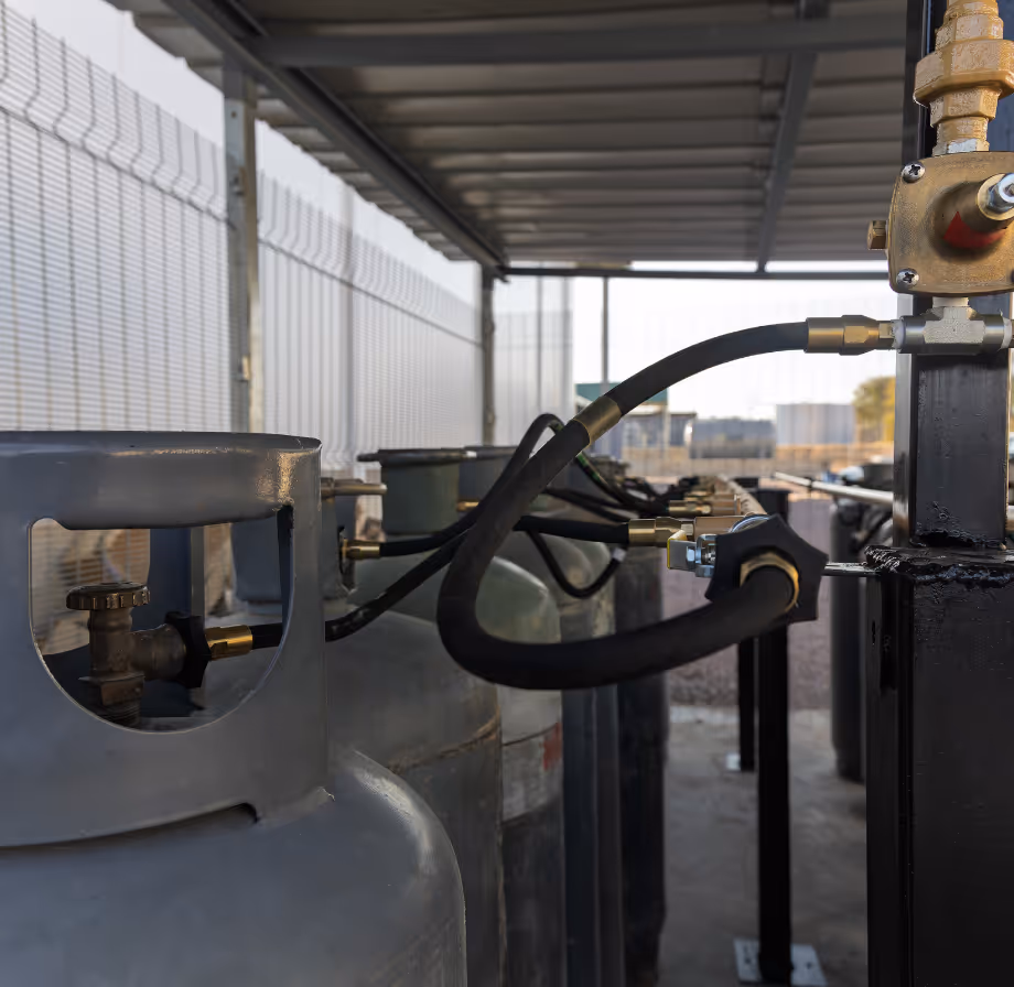 Row of connected industrial gas cylinders secured under a metal roof with black hoses.