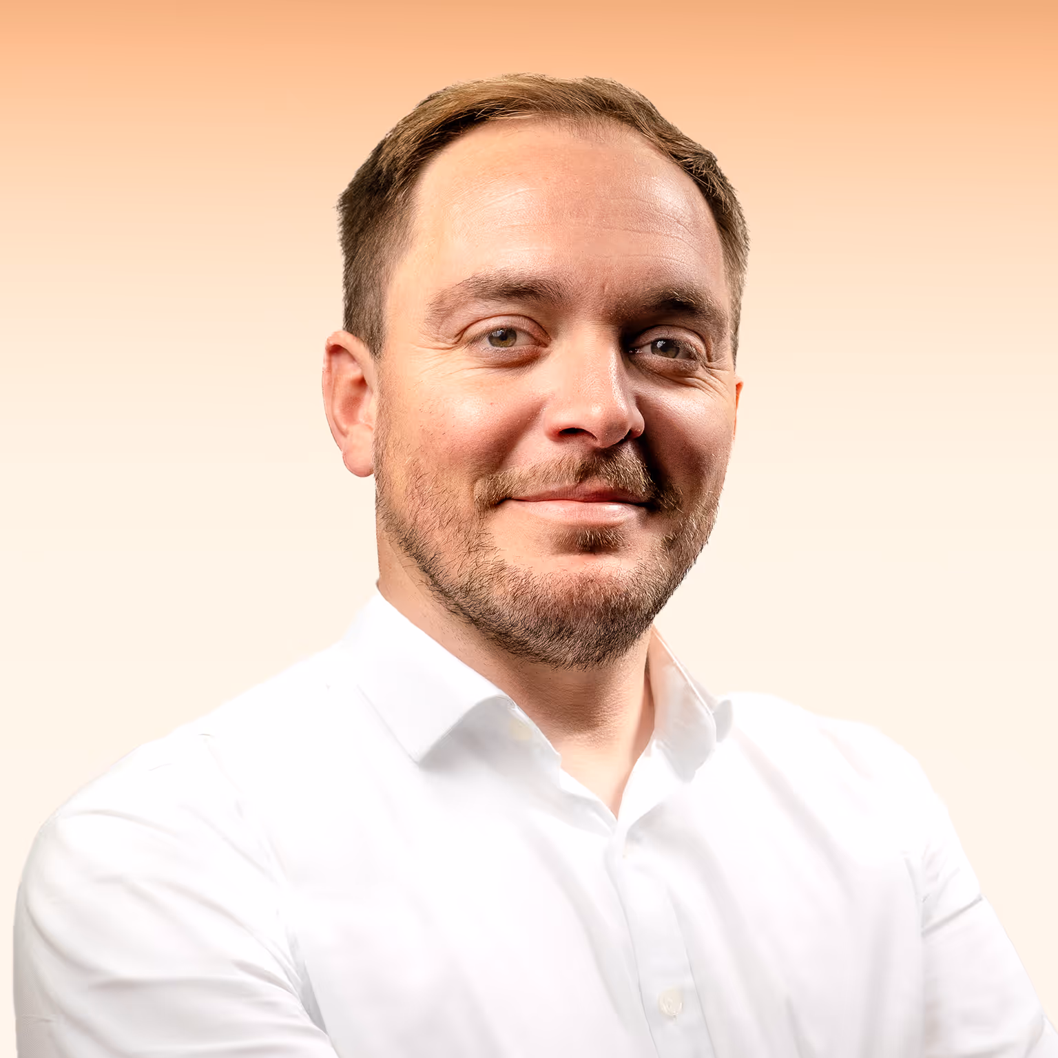 Smiling man with short brown hair and beard wearing a white button-up shirt against a light orange gradient background.