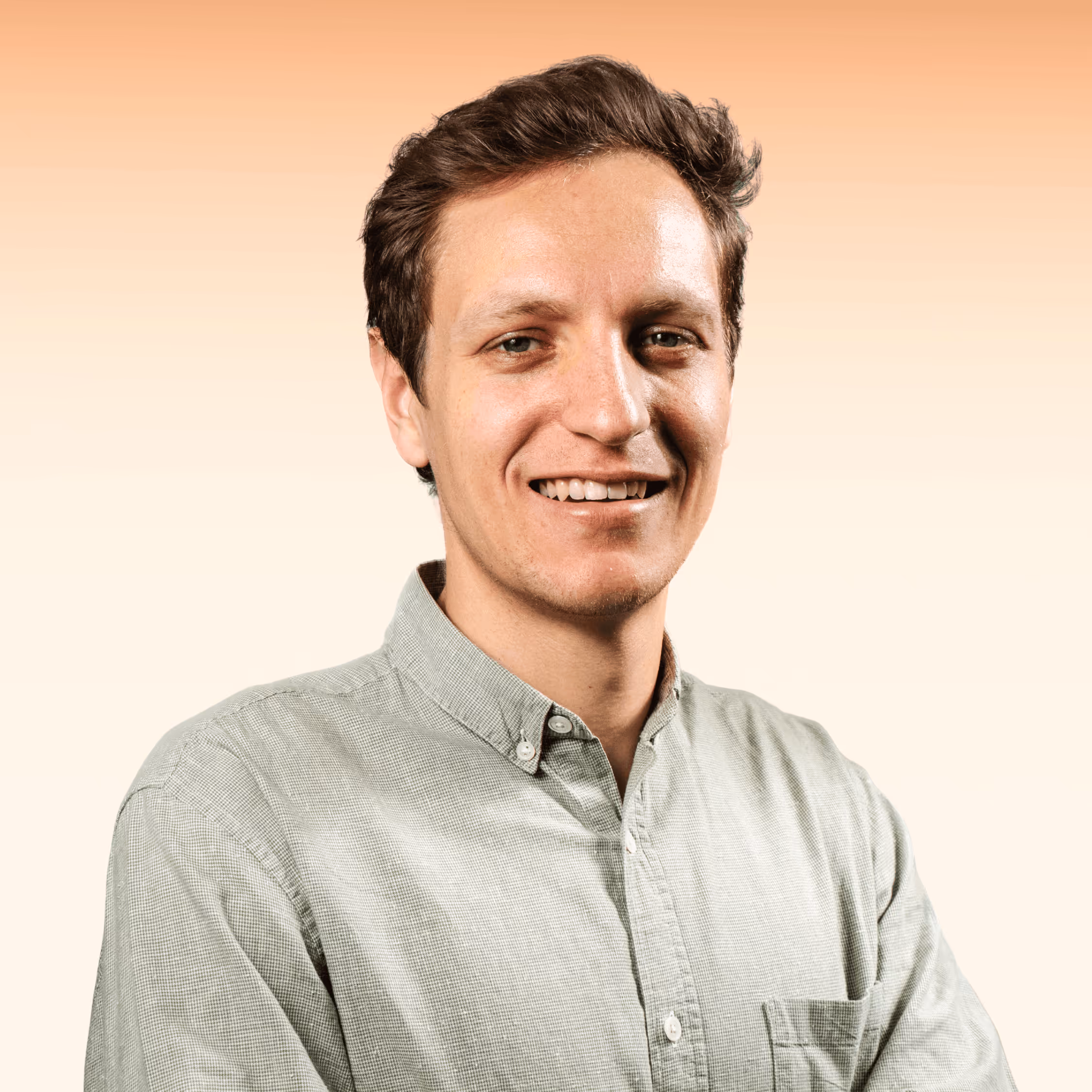 Smiling young man with short brown hair wearing a light green button-up shirt against a peach gradient background.