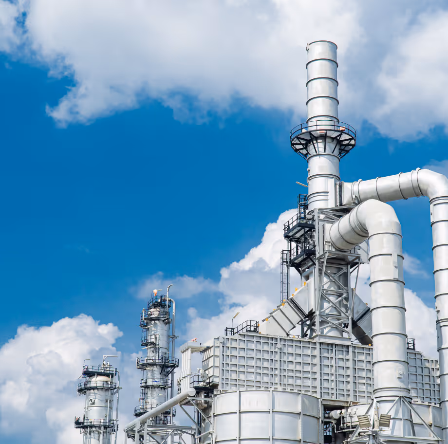 Industrial plant with large silver pipes and tall chimneys under a blue sky with clouds.