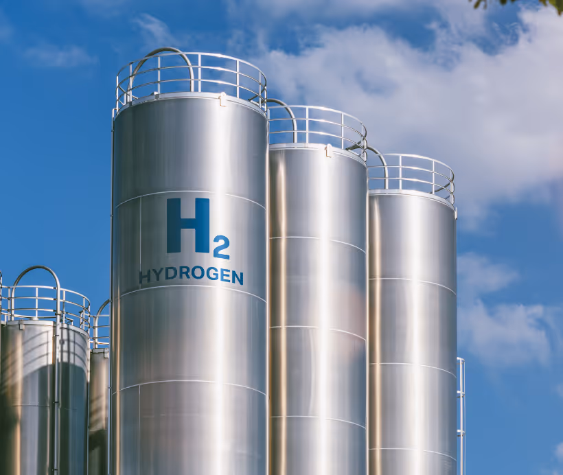 Group of people standing on grass field looking up at the base of a large wind turbine with clear blue sky.
