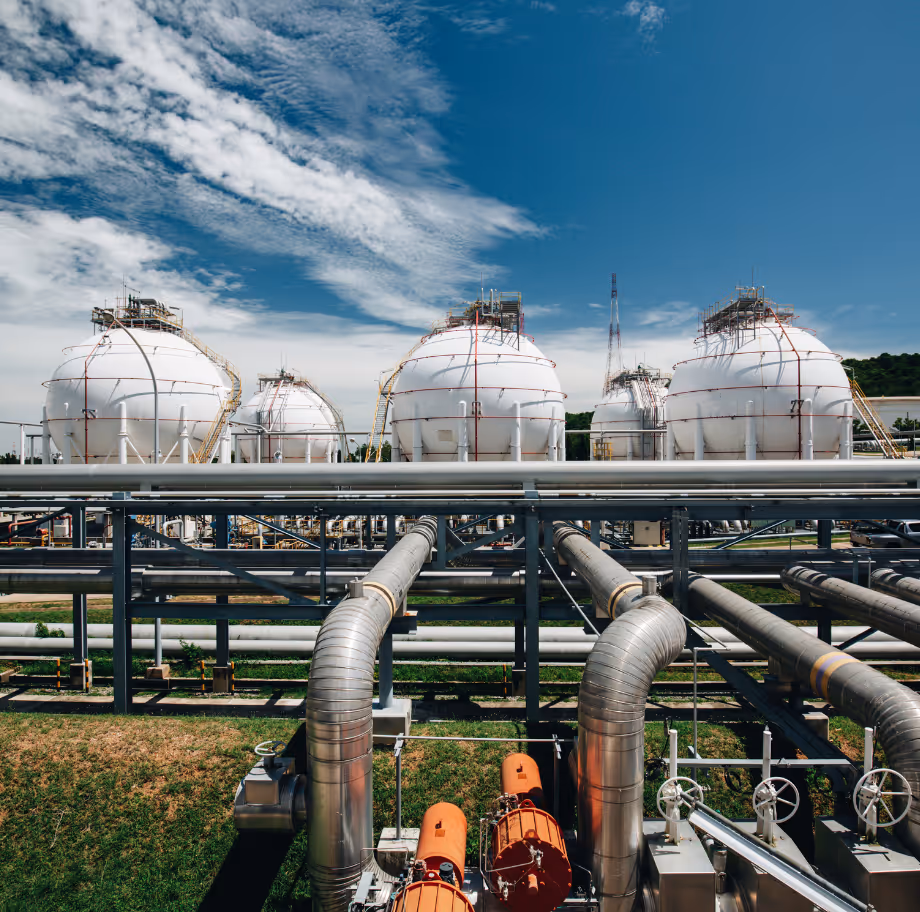 Industrial gas storage facility with large white spherical tanks and metal pipelines under a partly cloudy blue sky.