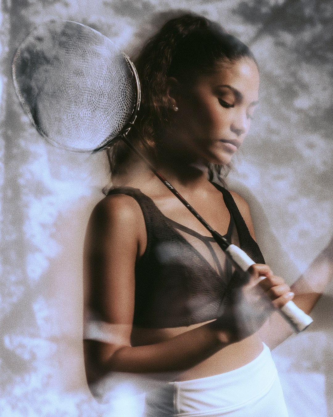 Woman in athletic wear holding a badminton racket over her shoulder with a soft, dreamy background. Decathlon Chantelle Sport Bra Laure Mimram