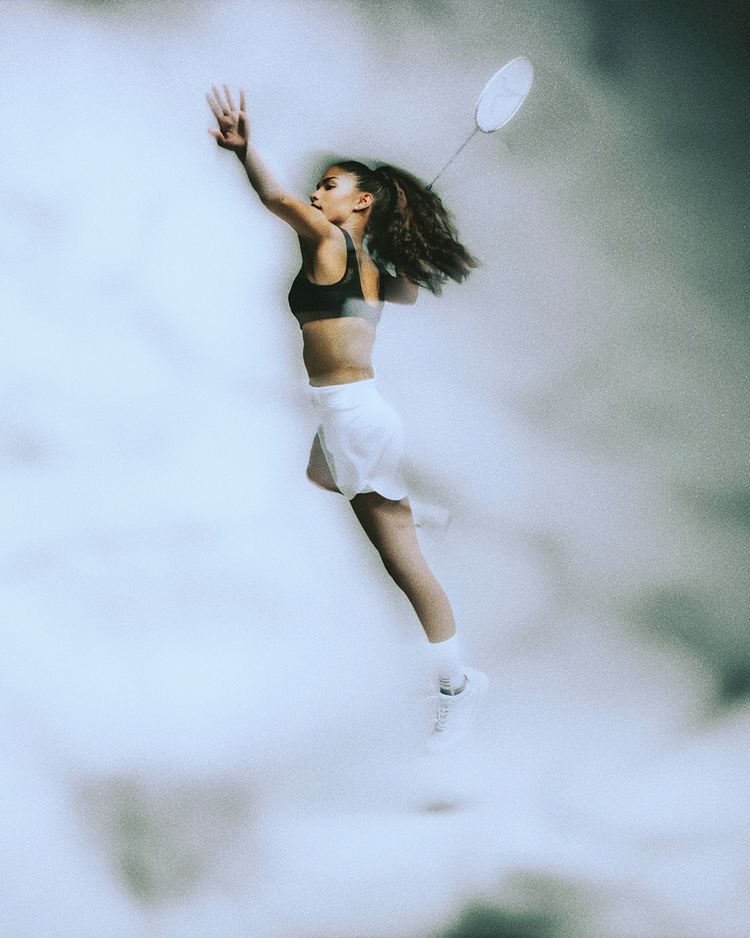 Young female badminton player in mid-air leap, preparing to hit a shuttlecock with racket. Decathlon Chantelle Sport Bra Laure Mimram