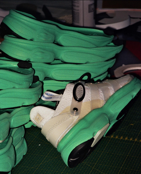 A close-up of a white sneaker with a bright green sole placed on top of multiple stacked green shoe soles on a cutting mat Decathlon Footwear Industrial Division FID Decathlon wwweshstudio Laure Mimram