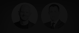Two men, one bald wearing a dark shirt, the other with dark hair in a suit and tie, both in circular frames on a dark background.