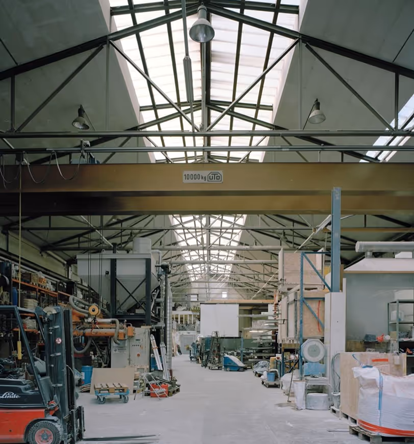 Interior of a spacious industrial warehouse with metal beams, a hoist labeled 10000 kg, machinery, and a forklift.