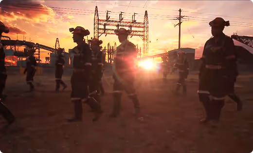 Silhouettes of workers walking in an industrial area during sunset with electrical infrastructure and power lines in the background.