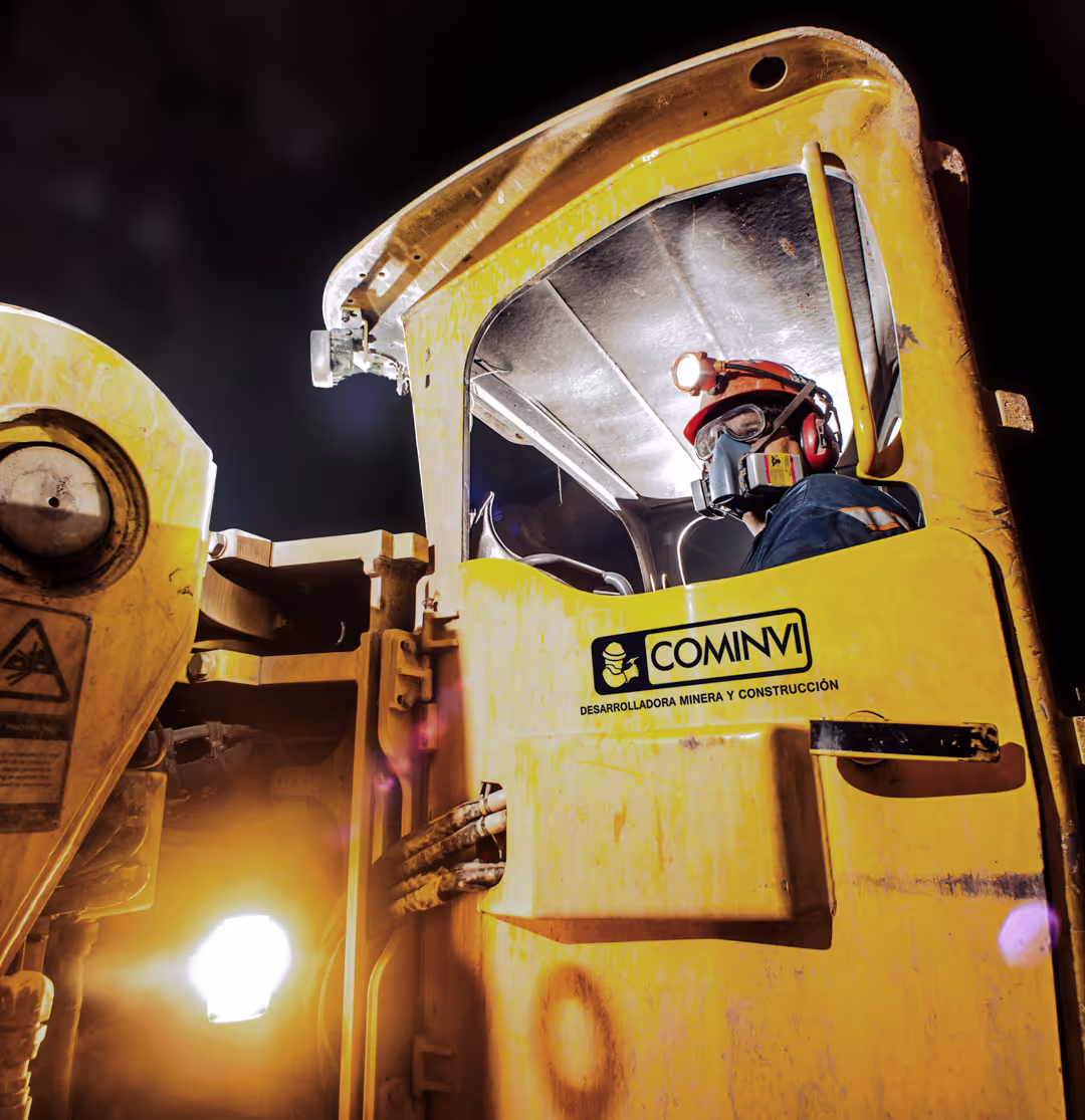 Worker wearing protective gear operating yellow mining equipment with COMINVI logo at night.