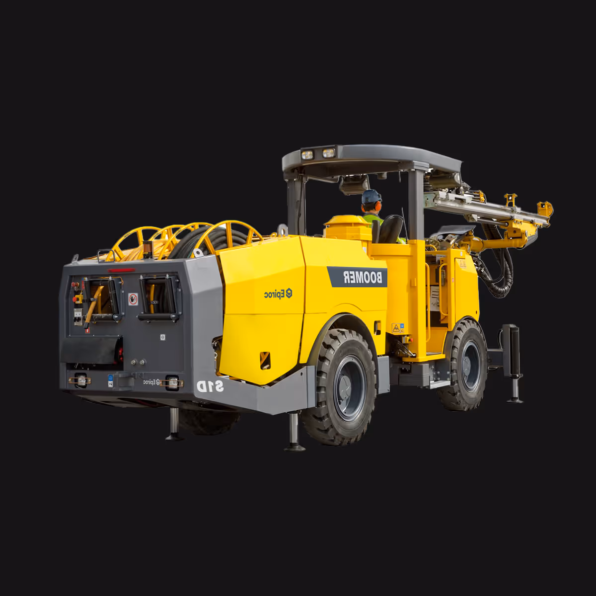 Yellow drilling rig vehicle labeled 'BOOMER' with a seated operator wearing a helmet and ear protection.