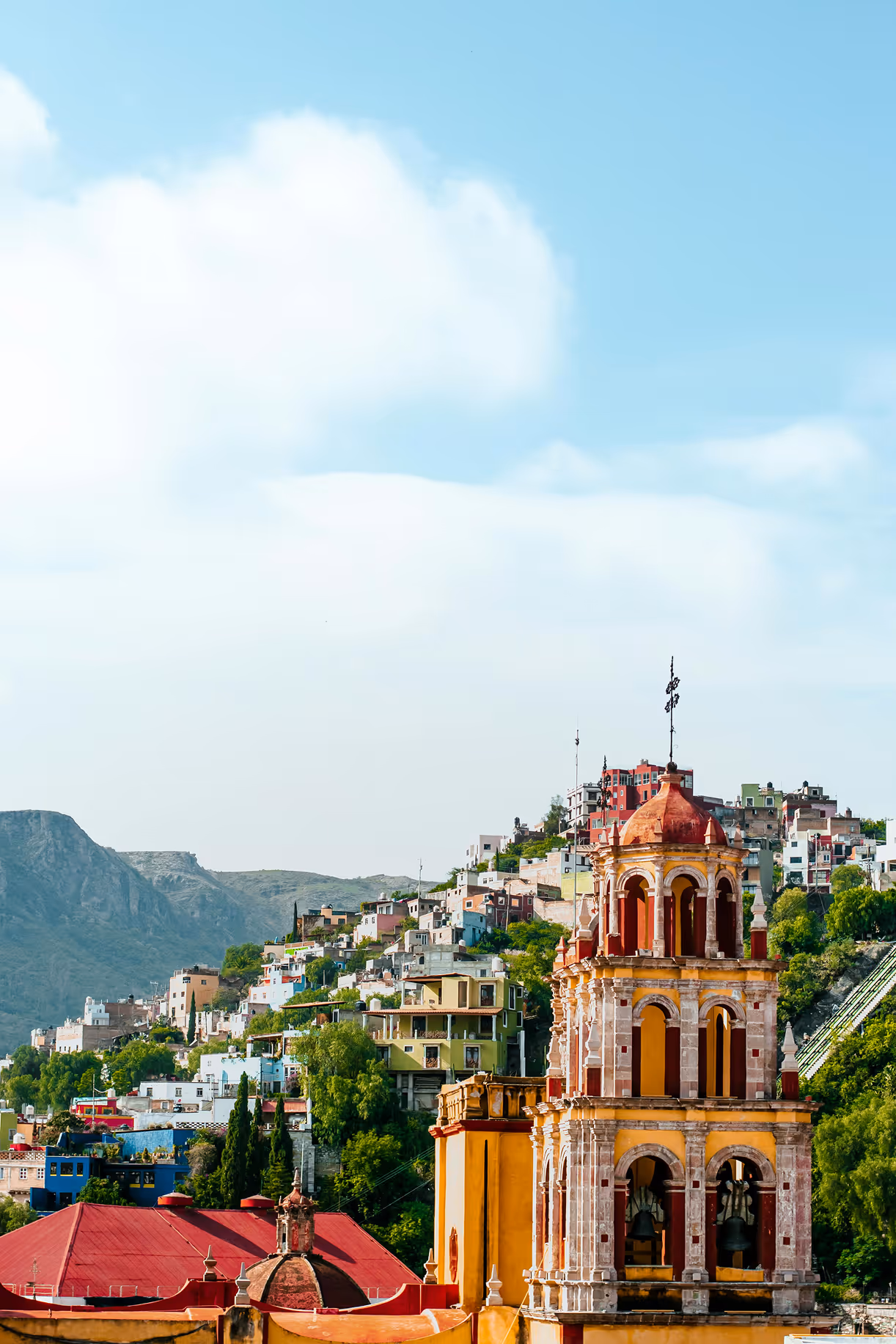 Colorful houses on a hillside with a historic bell tower in front under a partly cloudy sky.