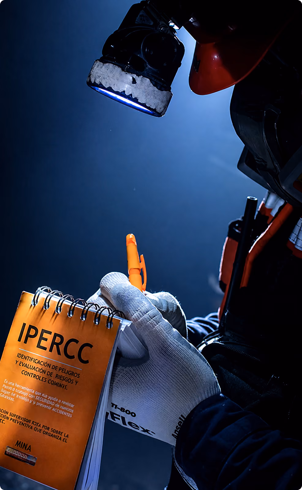 Worker wearing gloves and helmet writes on an IPERCC safety checklist under bright light.