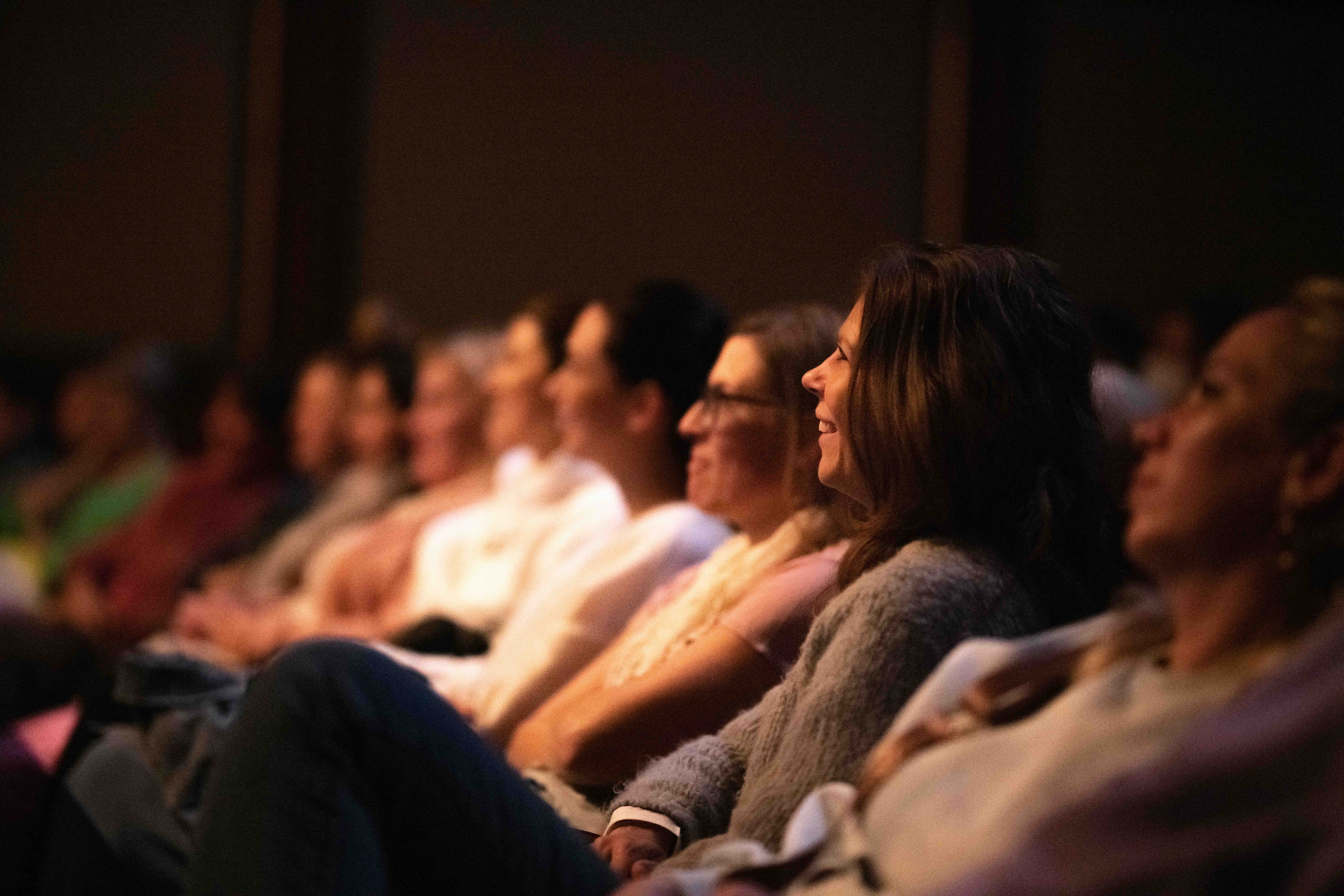 A woman smiles in the audience during a performance.