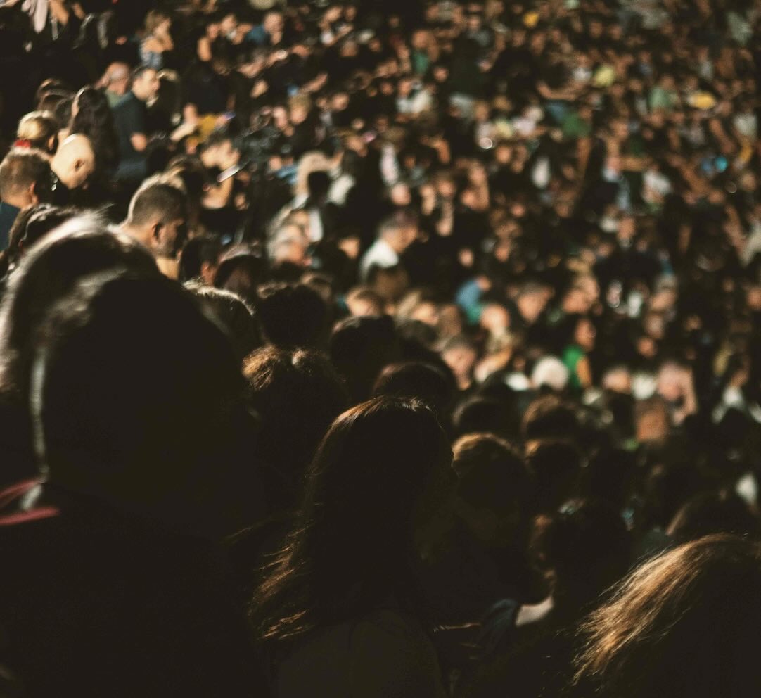 A large audience seated closely together in a dimly lit hall or arena during an event.