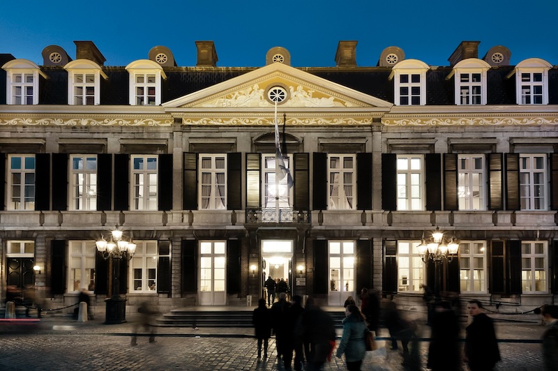 De verlichte voorgevel van Theater aan het Vrijthof in Maastricht bij avond, met voorbijlopende bezoekers op het plein ervoor.