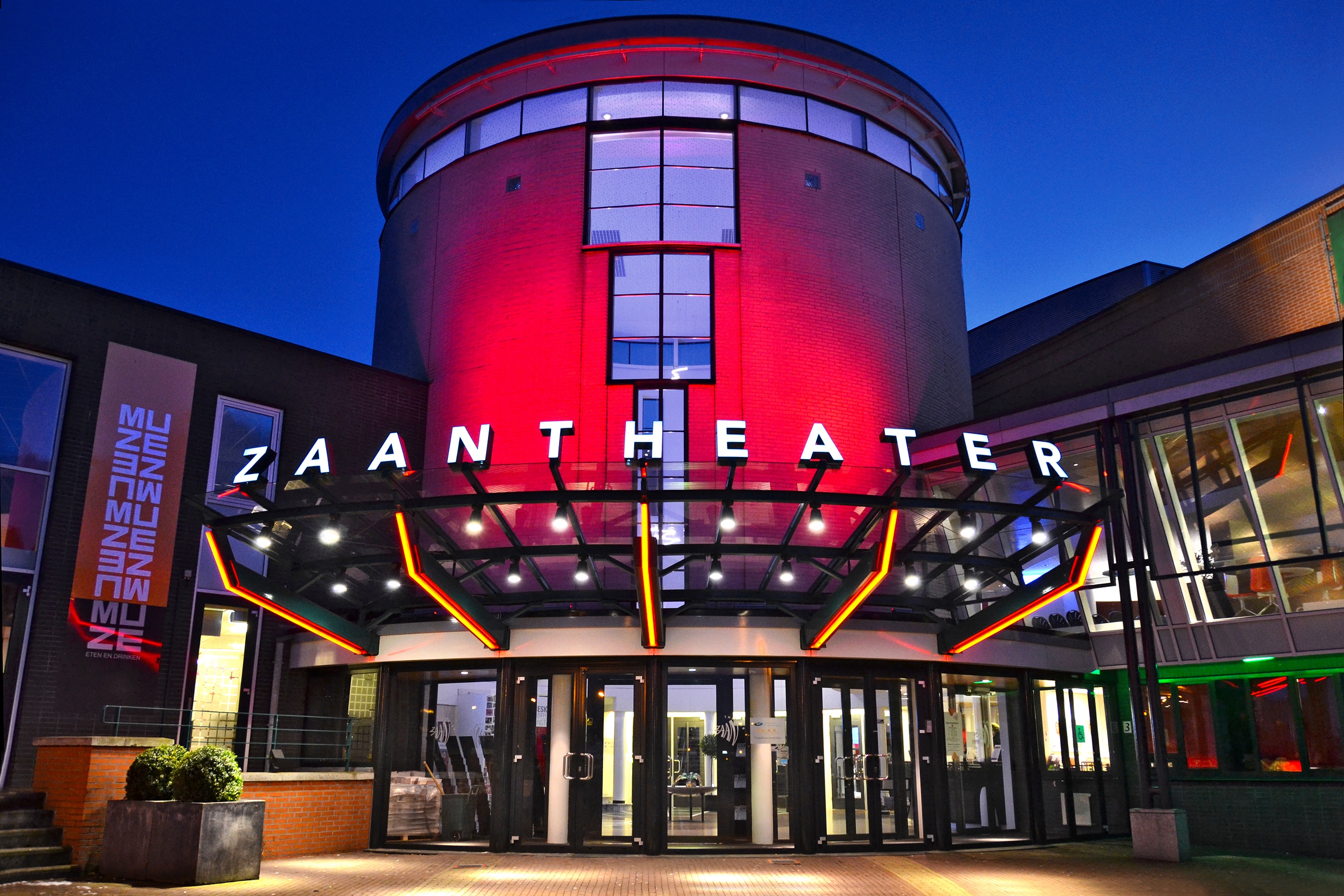 The illuminated facade and entrance of the Zaantheater at dusk.