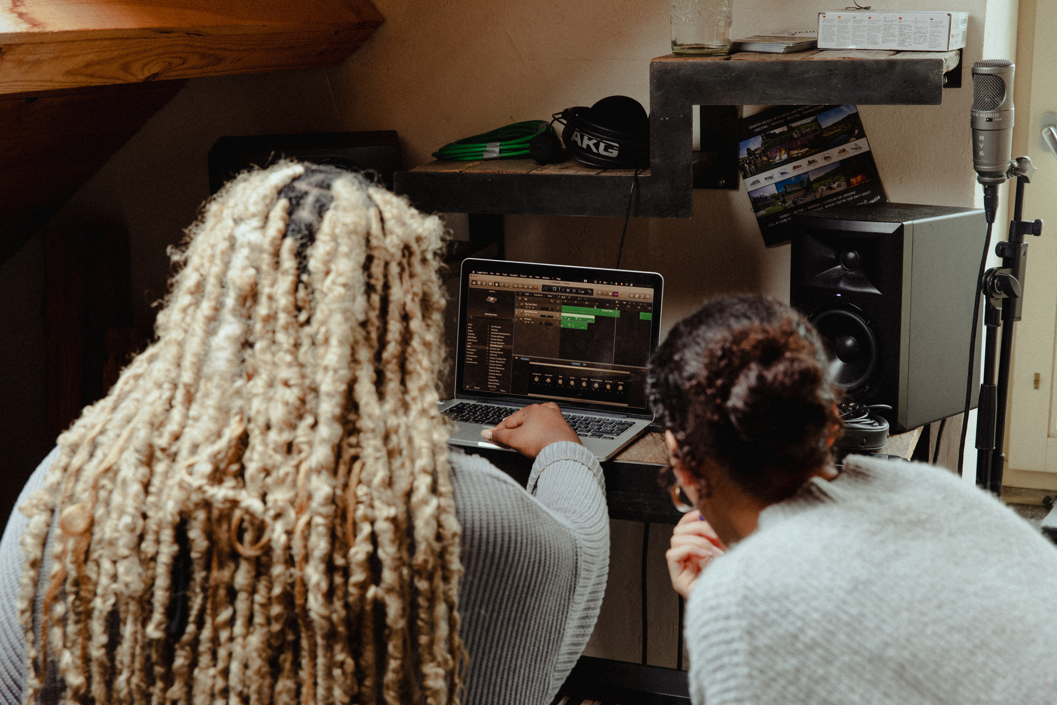 Deux jeunes musiciens travaillent ensemble sur un morceau sur un ordinateur portable dans un petit home studio avec micro et enceintes.