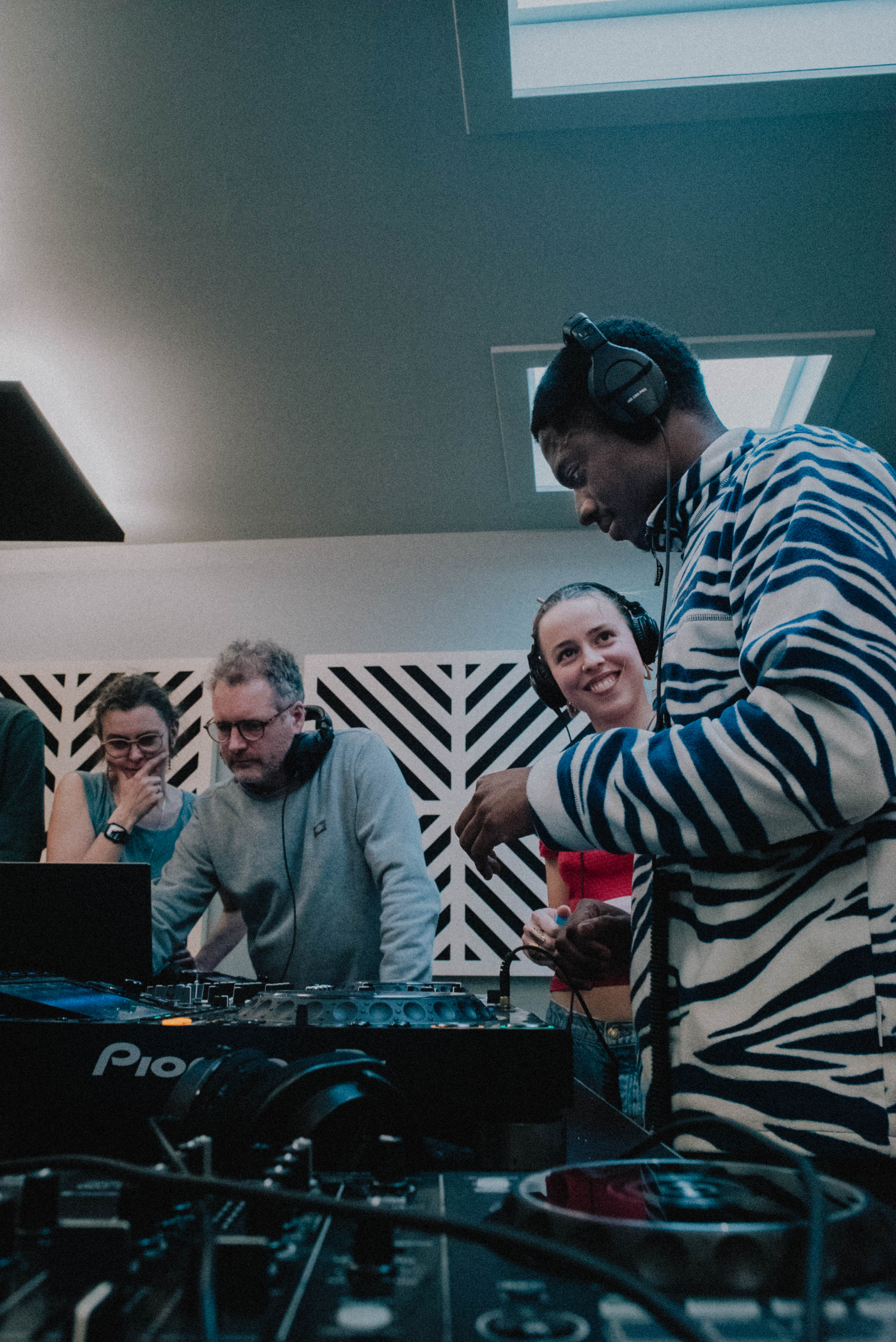 Groupe de jeunes musiciens et producteurs écoutant de la musique et travaillant sur un set DJ dans un studio avec du matériel de DJ et des casques.