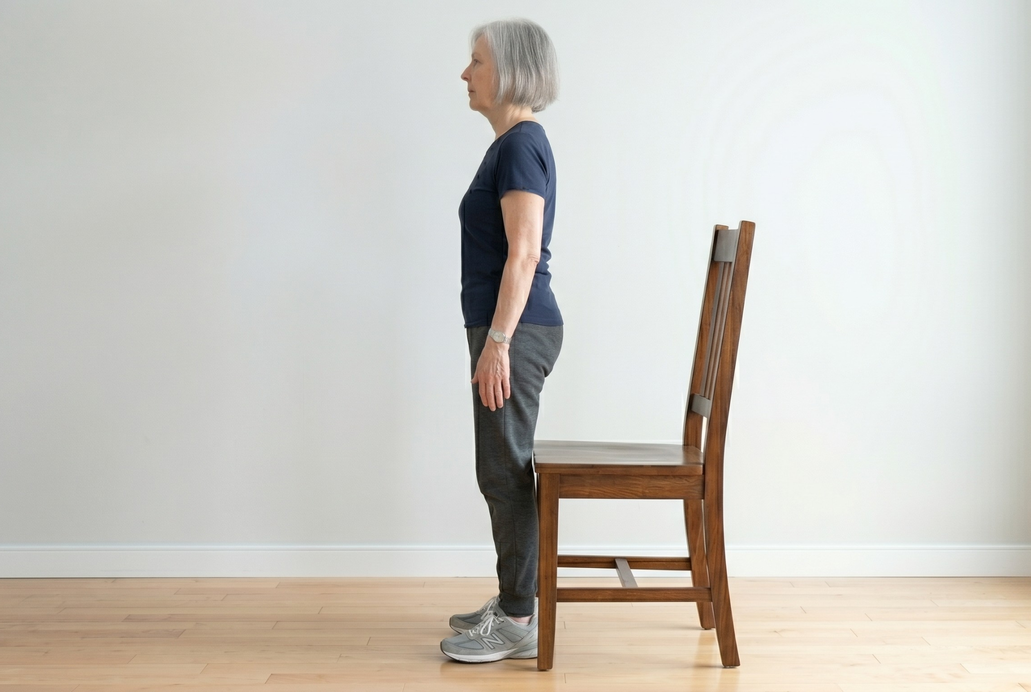 Older woman standing fully upright beside a chair at the end of a sit-to-stand exercise