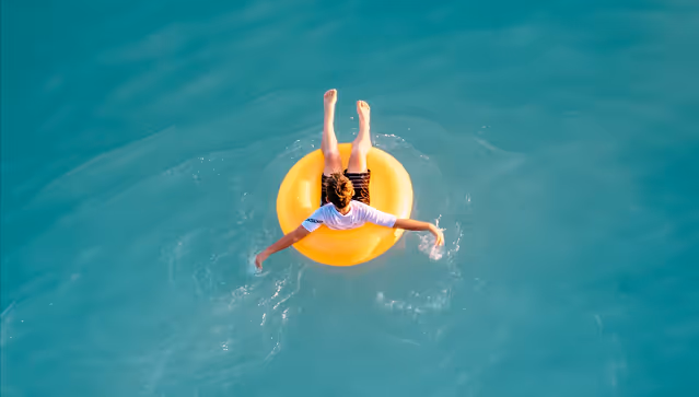 Person floating on a yellow tube in clear turquoise water, viewed from above.