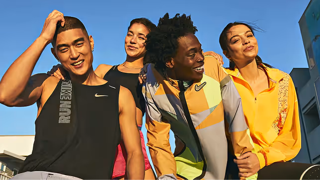 Group of four diverse young athletes in Nike sportswear smiling and posing outdoors in sunlight.