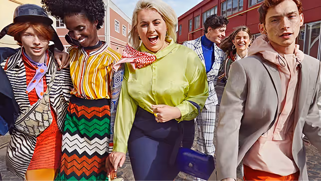Group of six diverse young adults walking outdoors, dressed in vibrant, fashionable clothing and smiling.