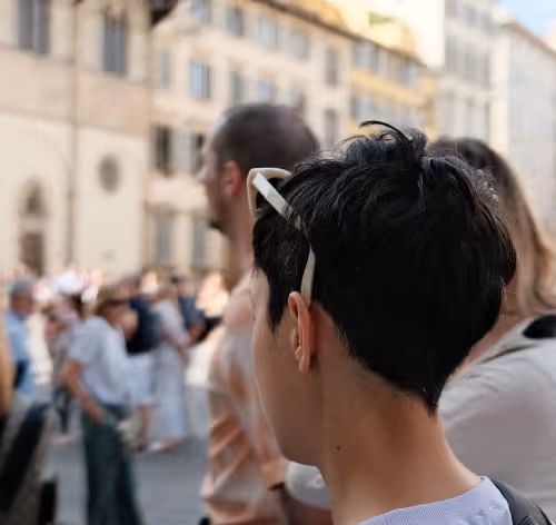 Person with short dark hair and white sunglasses on head facing away in a crowded urban setting.