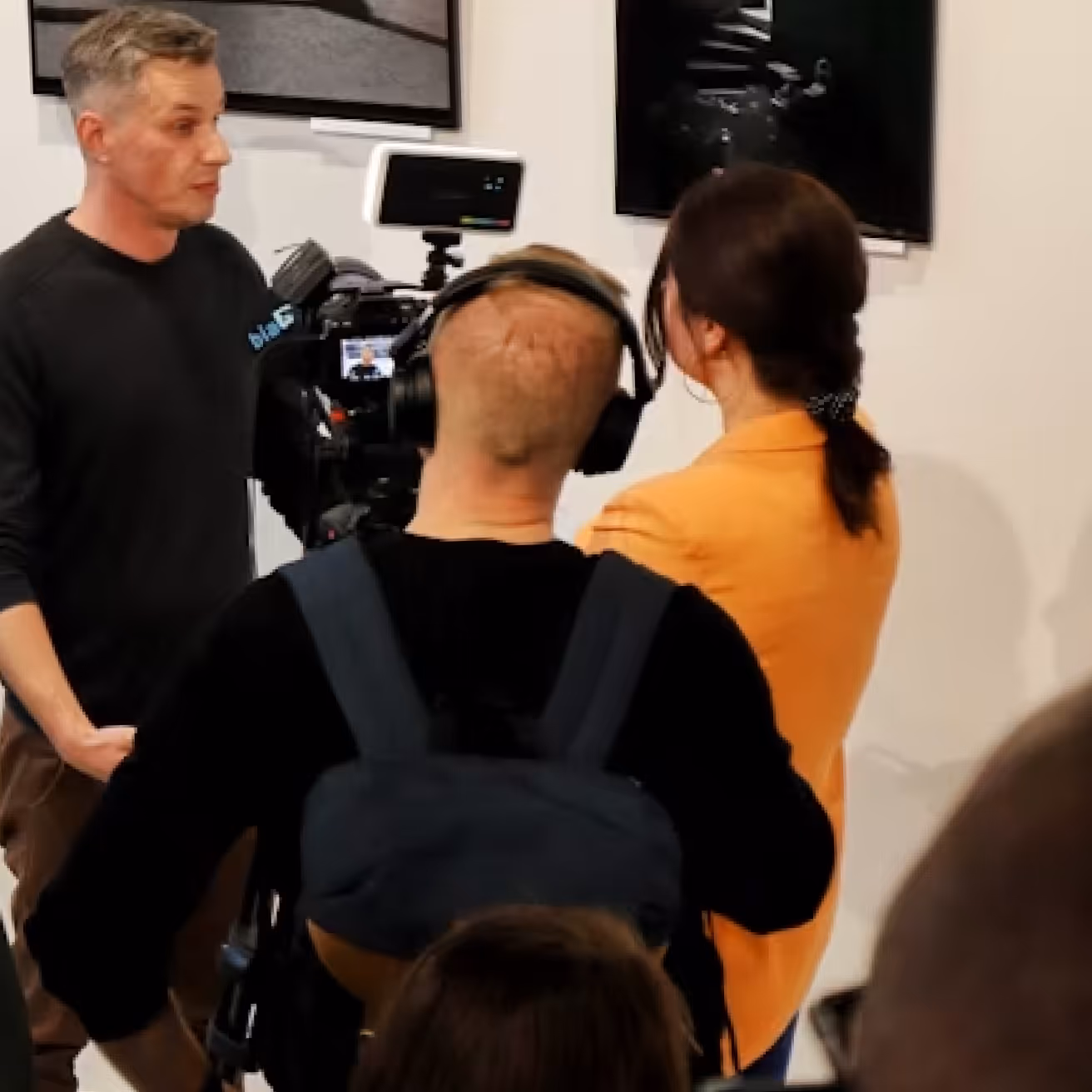 Filming crew with a camera and monitor recording a man speaking indoors.