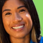 Close-up of a smiling woman with medium skin tone and dark hair against a green background.