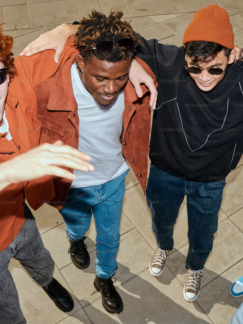 Overhead view of three friends walking with arms around each other, smiling and wearing casual clothes.