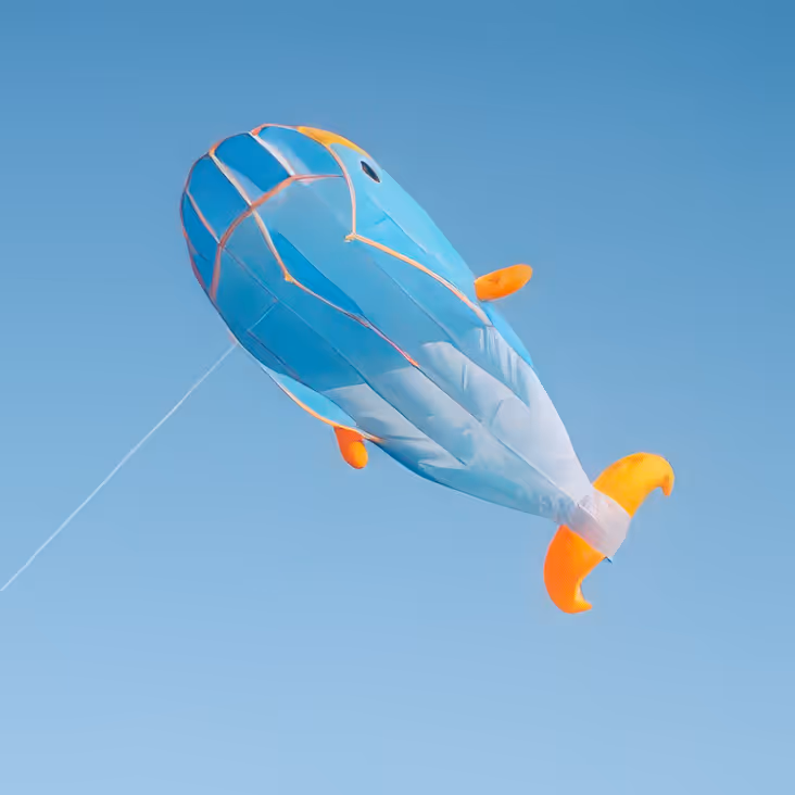Blue and orange whale-shaped kite flying against a clear blue sky.