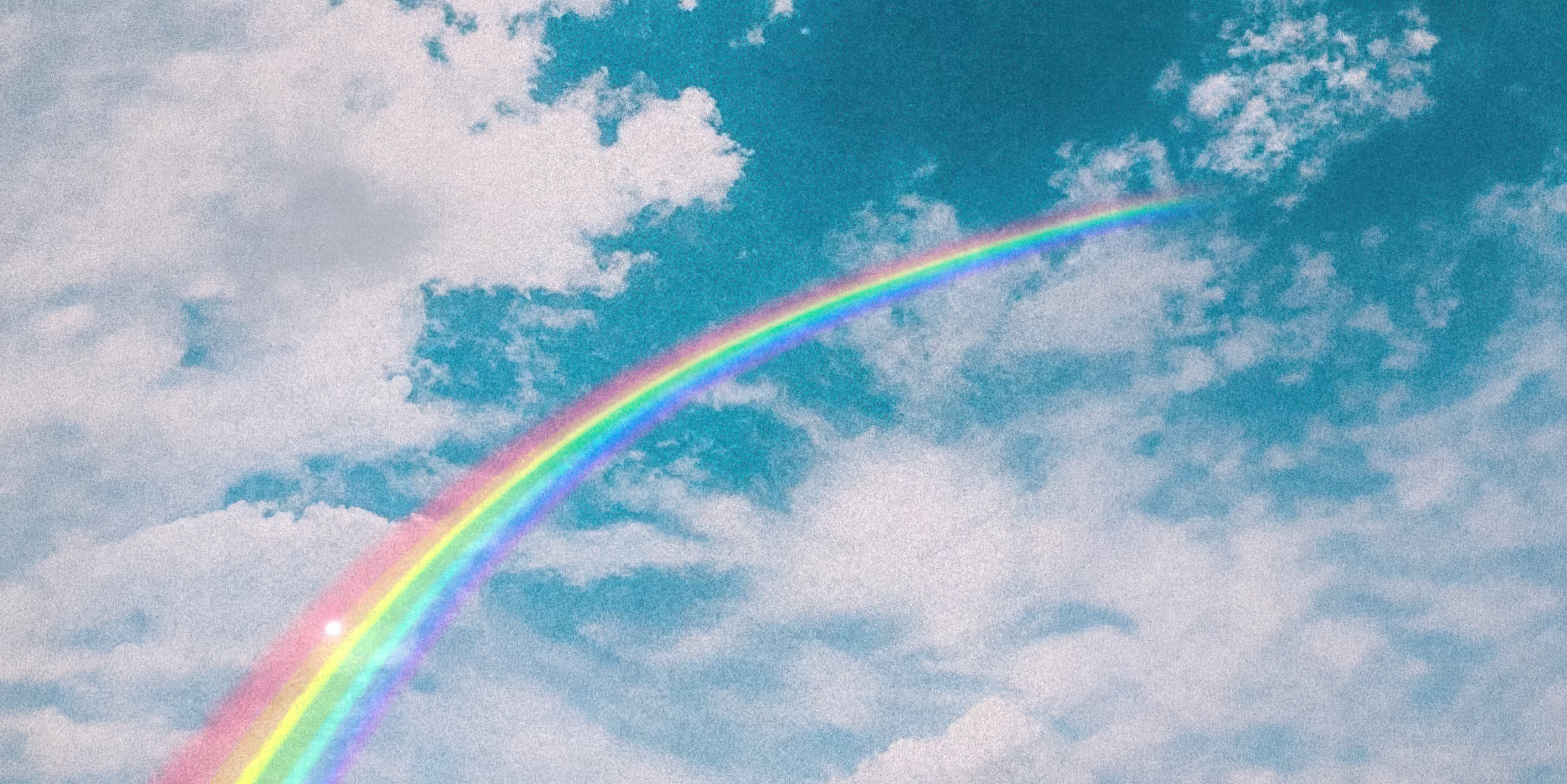Bright rainbow arching across a blue sky with scattered white clouds.