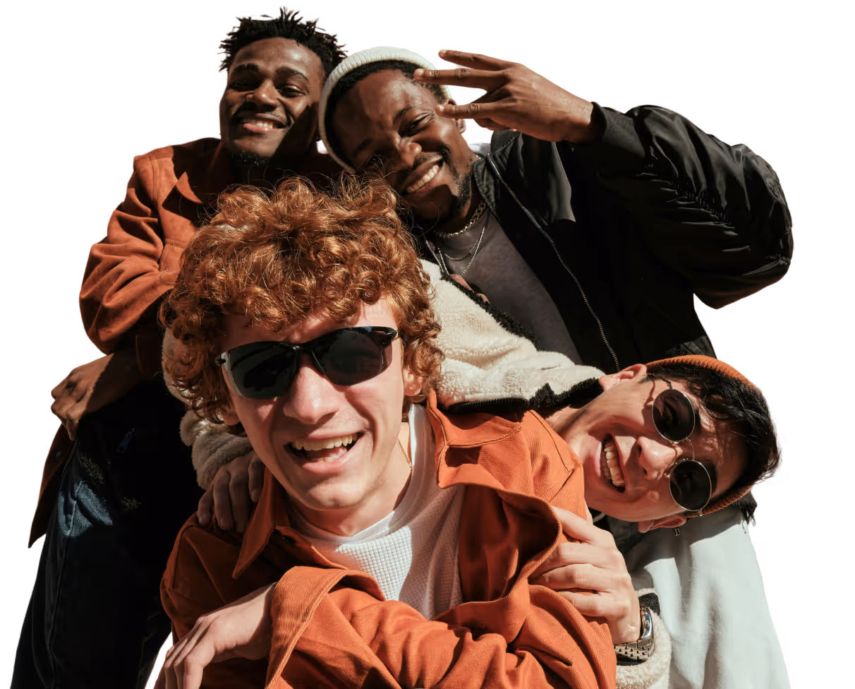 Four diverse young men smiling and posing closely together, two wearing sunglasses and warm jackets.