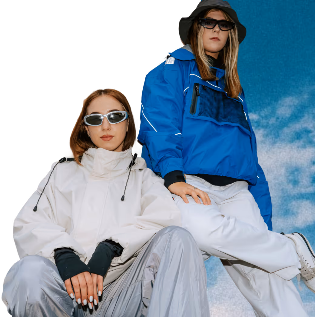 Two women wearing techwear jackets and sunglasses posing against a blue sky background.
