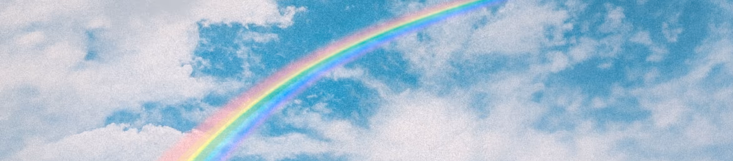 Colorful rainbow arching through a bright blue sky with scattered white clouds.